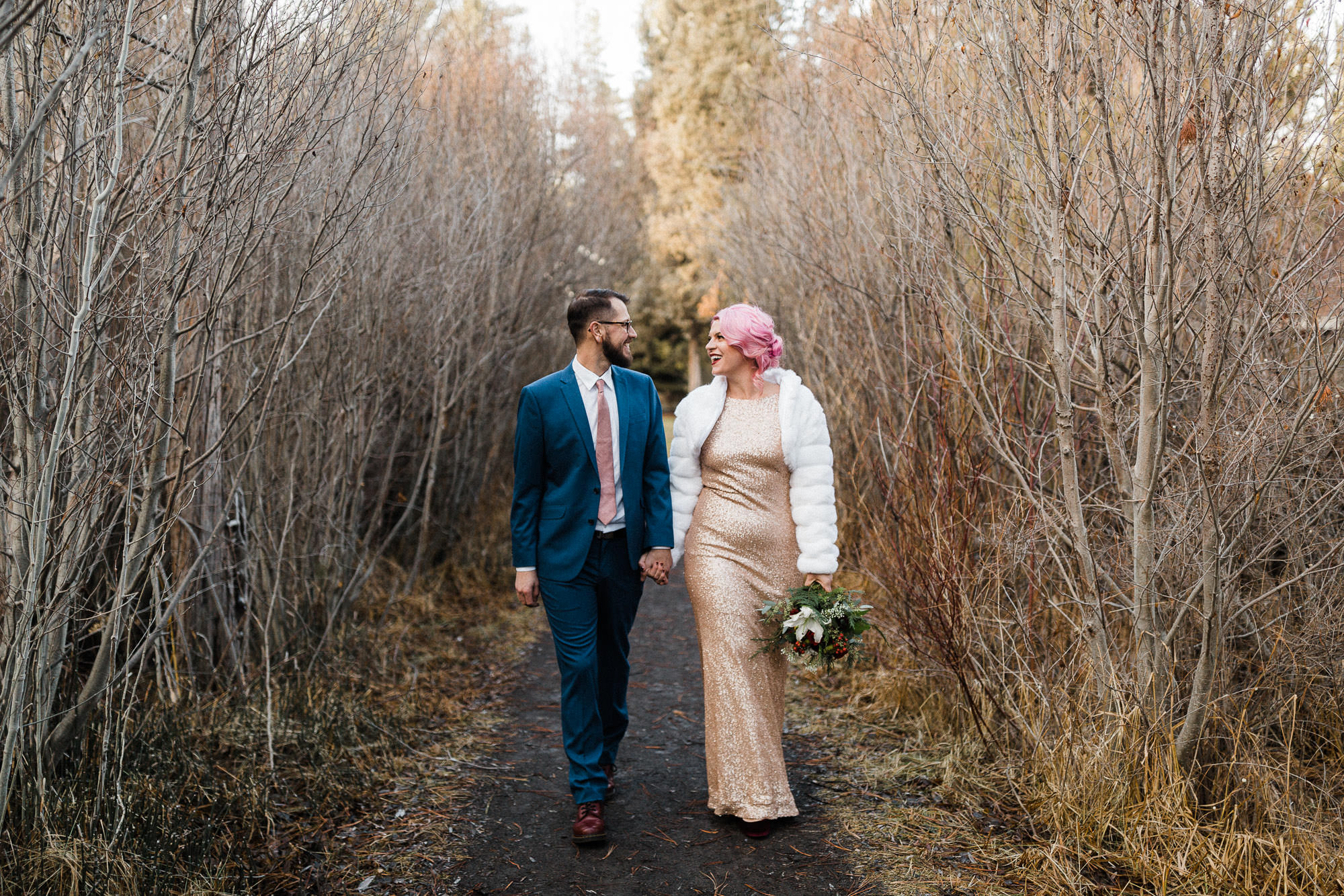 Bride and groom walk down path through dead trees in Bend, Oregon