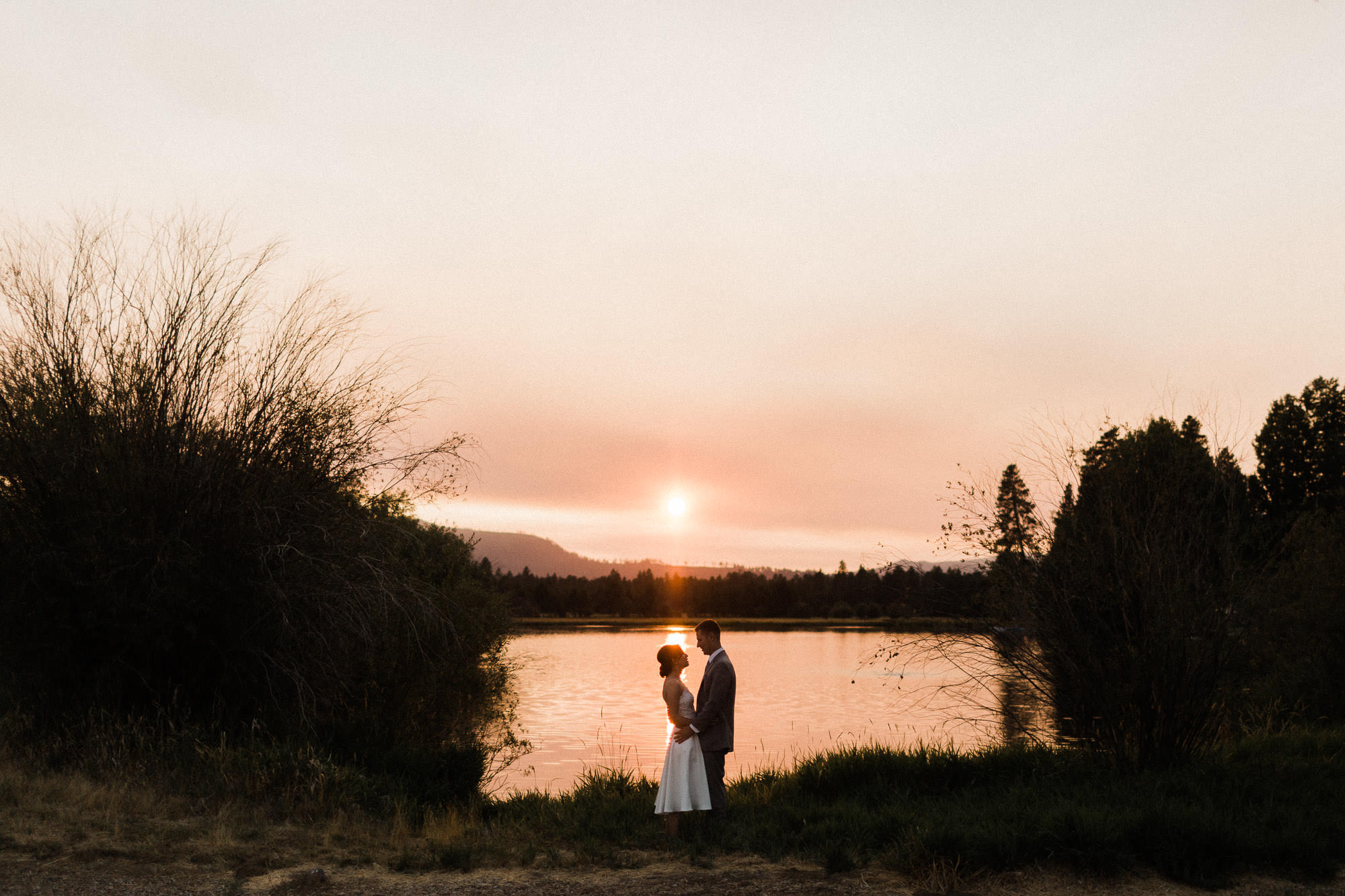 A bride and groom embrace in front of a pond at sunset at Black Butte Ranch