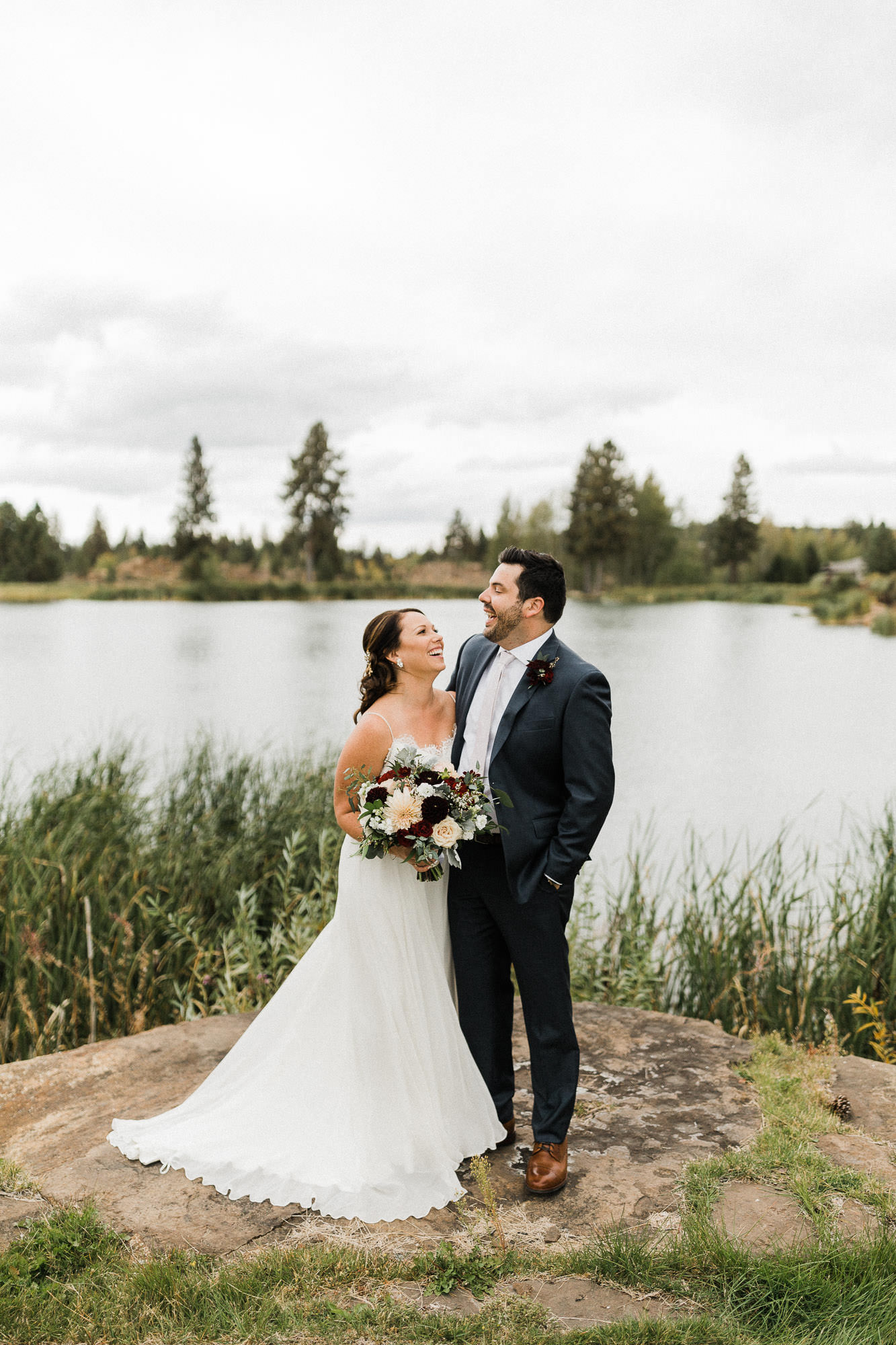 Bride and groom laugh in front of pond at Broken Top Club in Bend, Oregon