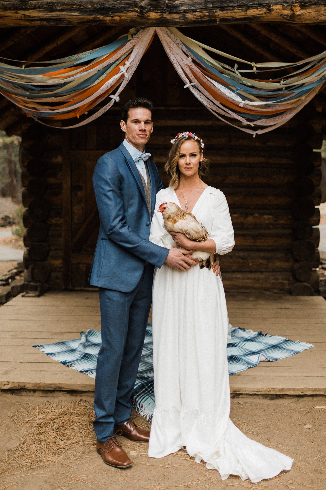 Bride and groom pose with chicken in front of cabin at High Desert Museum in Bend, Oregon