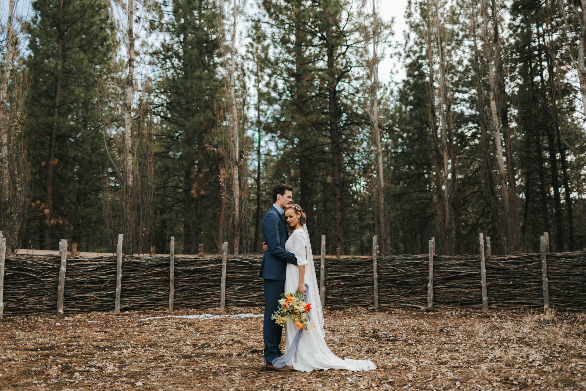 Bride and groom embrace in front of rustic fence at High Desert Museum in Bend, Oregon