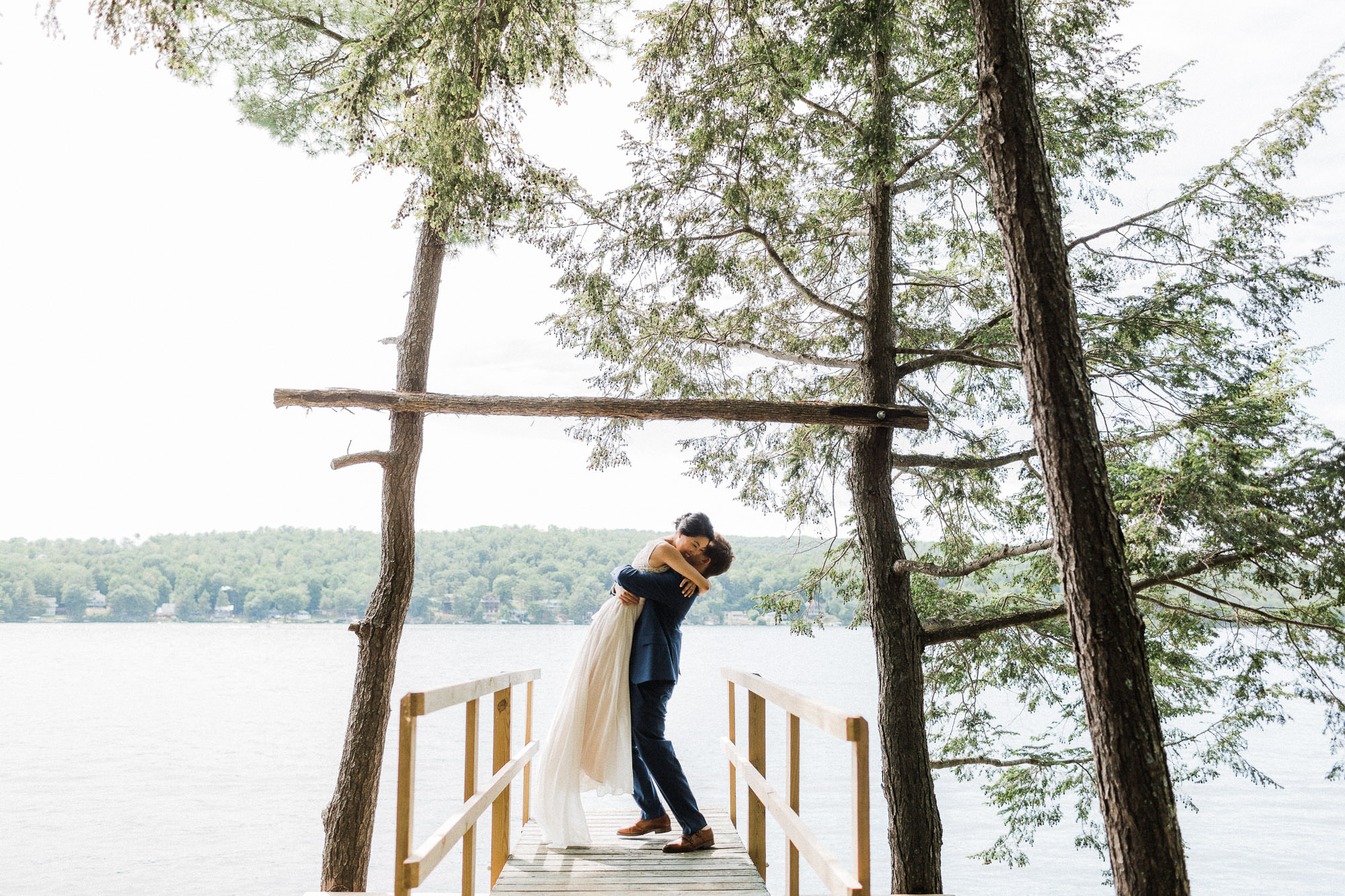 Groom lifts bride in the air with a hug on a dock at Lake Bomoseen in Vermont