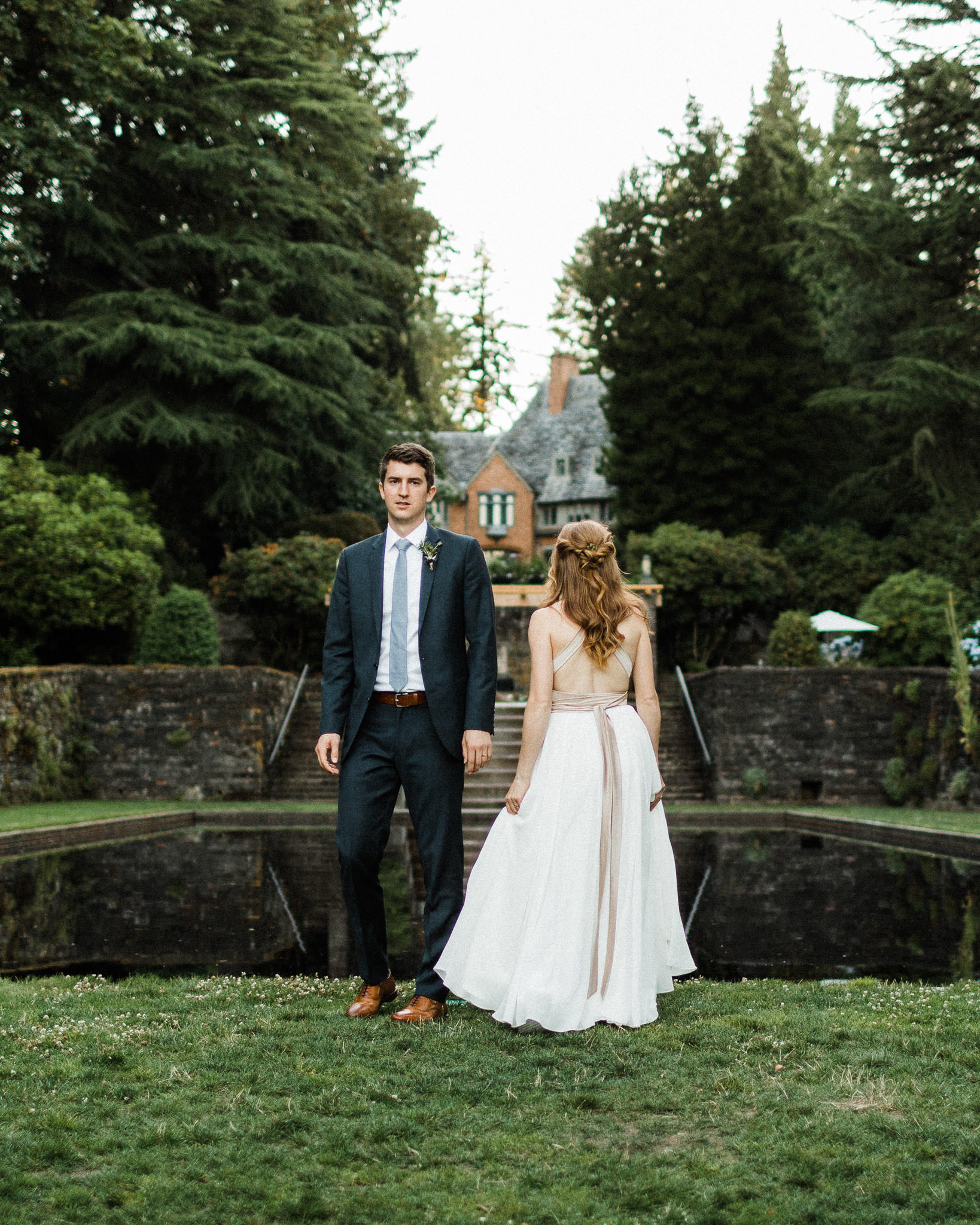 Groom and bride stand in front of the reflecting pool at Lewis and Clark College