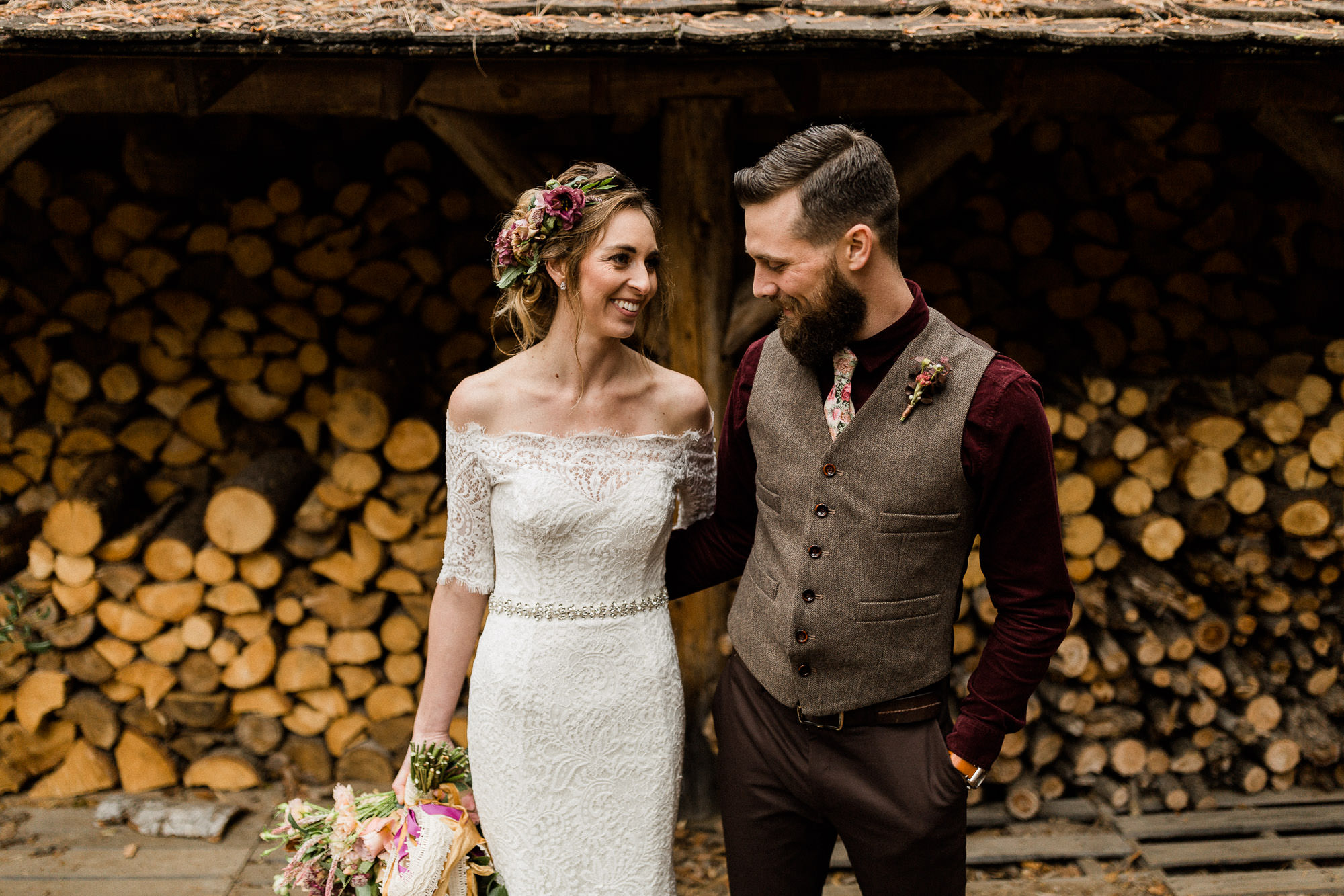 Bride and groom laugh in front of firewood stacks at Skyliner Lodge in Bend, Oregon