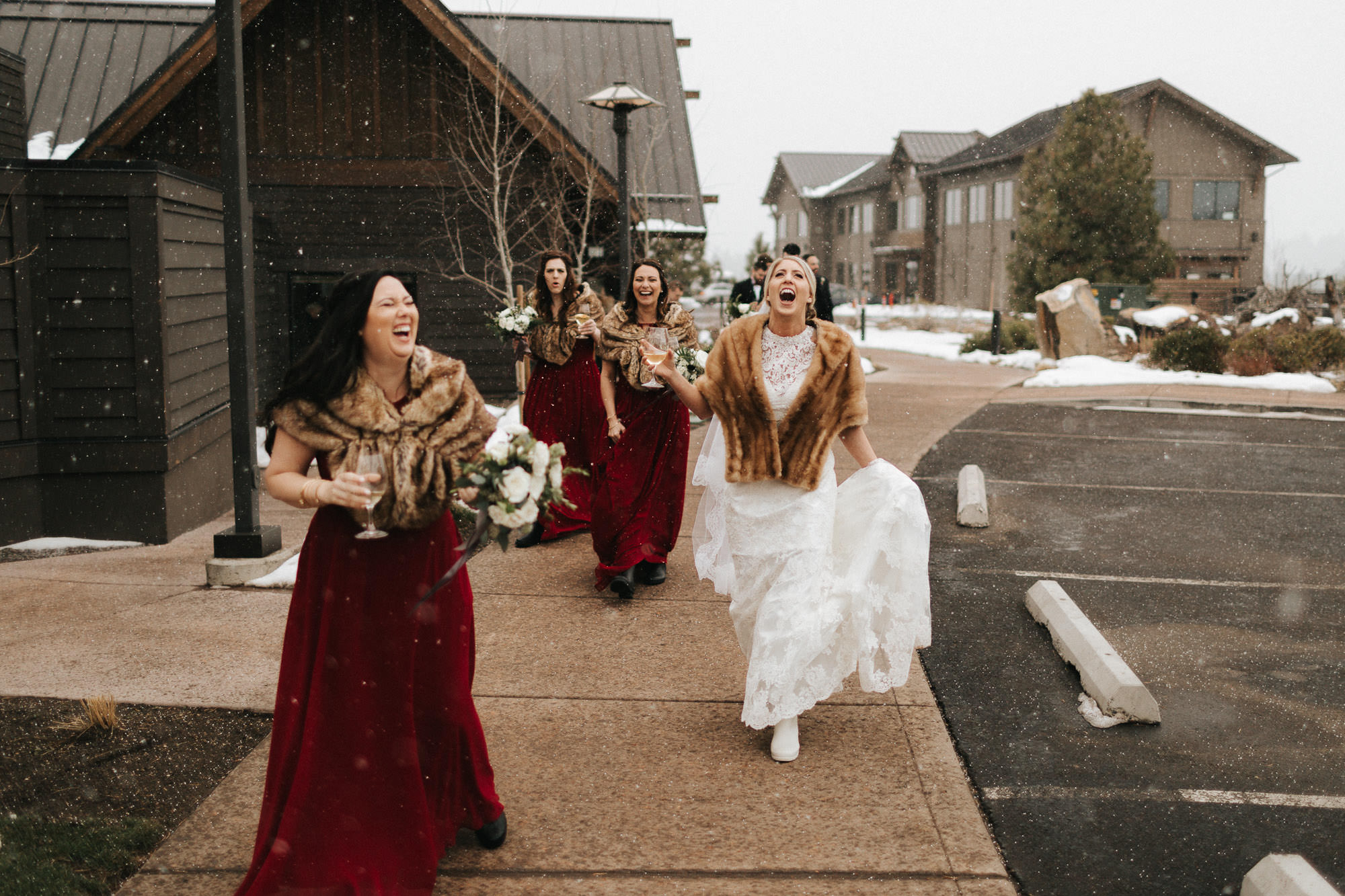 Bride and bridesmaids walk through falling snow at Tetherow in Bend, Oregon