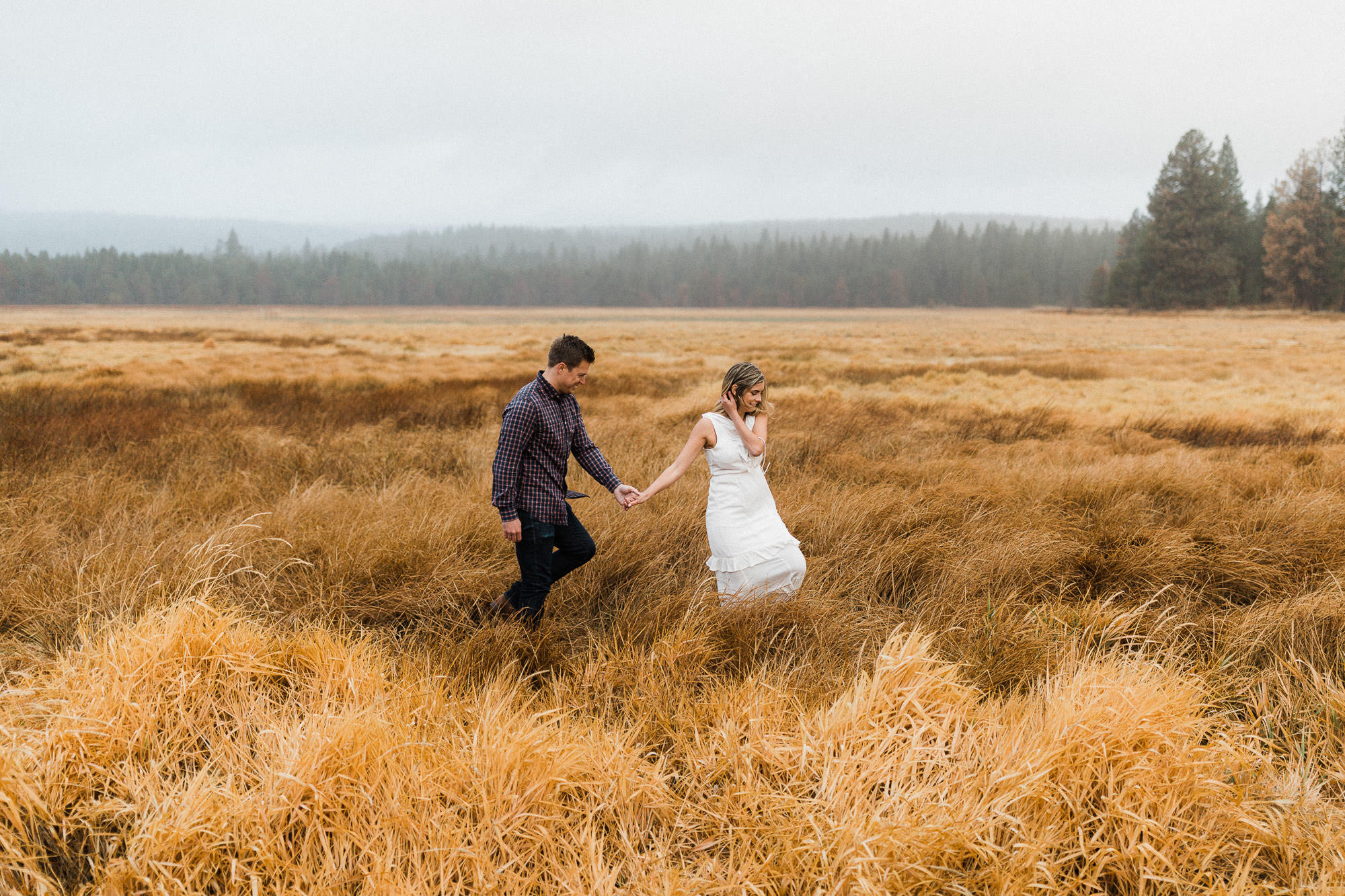 A couple walks through a field of dry grass along the Deschutes River in Bend, Oregon