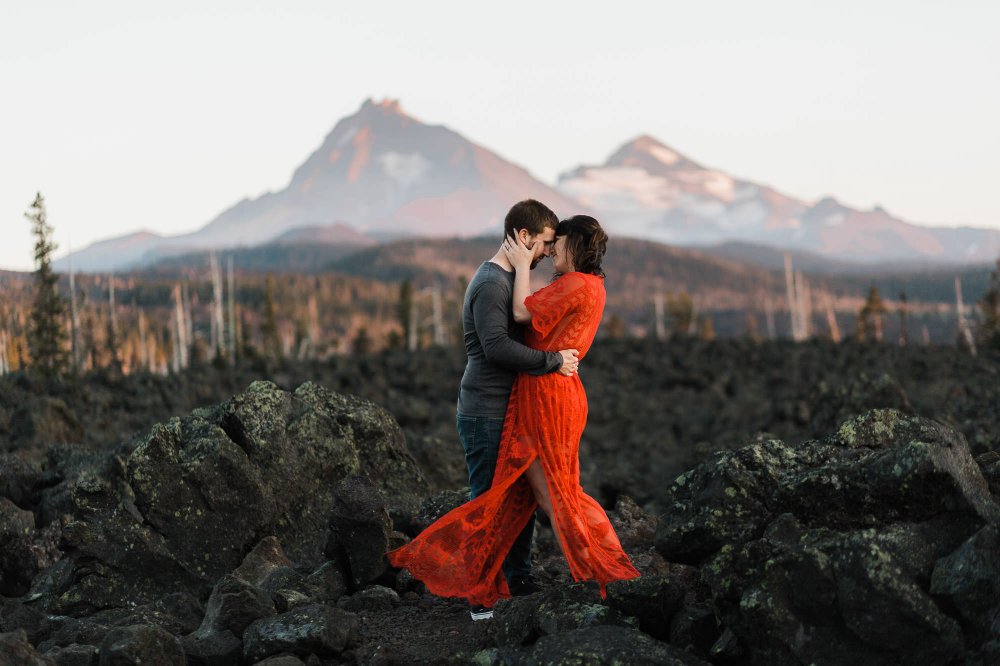 A couple embraces in a lava field with mountain views at sunset at McKenzie Pass in Oregon