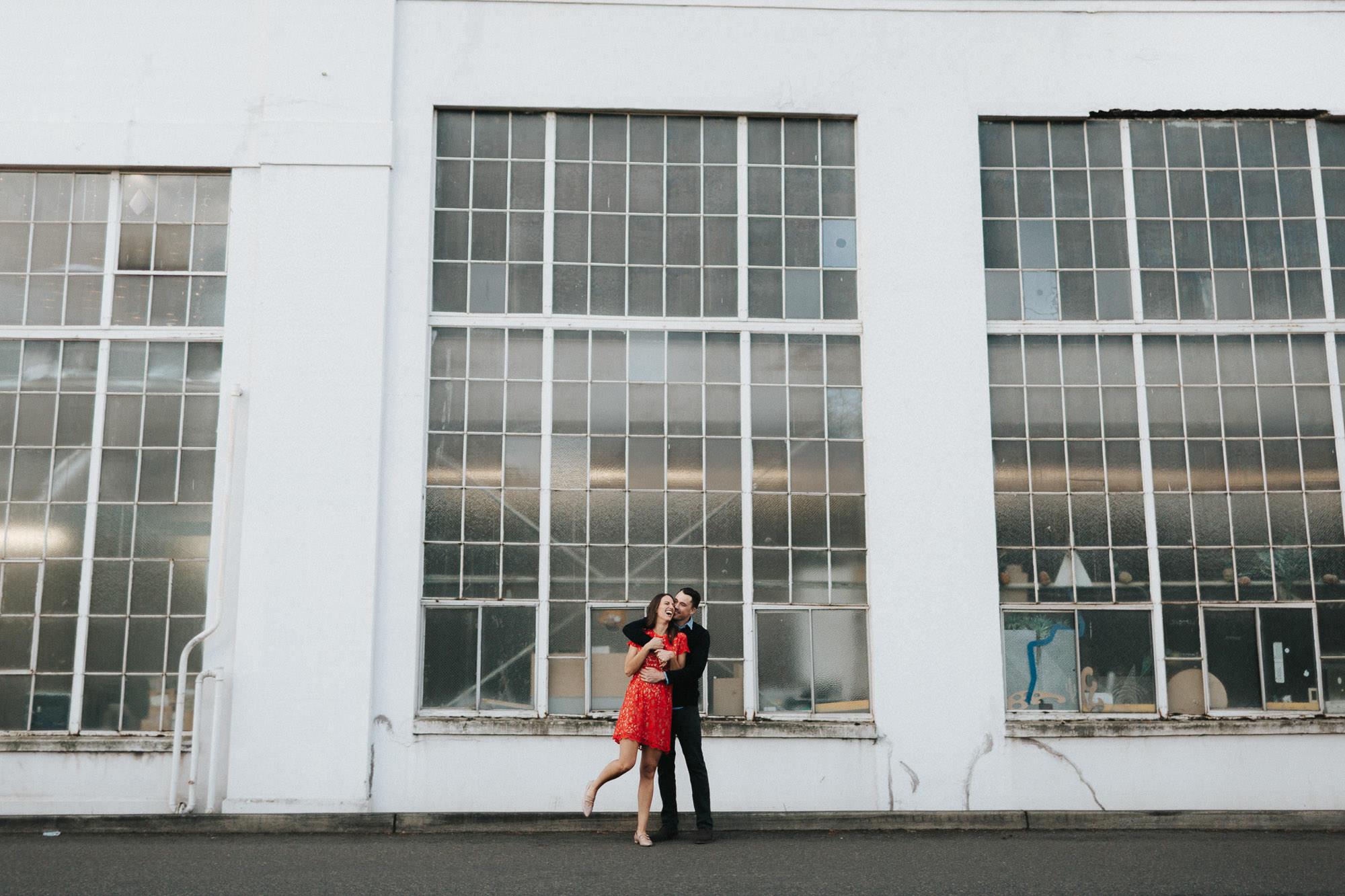 Couple laugh and embrace in front of industrial building in Portland, Oregon