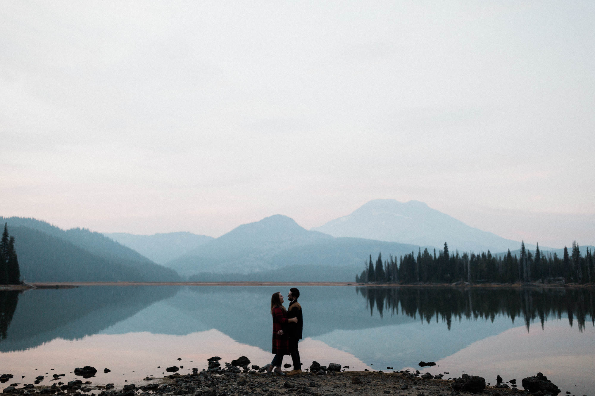 A couple embraces in front of mountain views on the shores of Sparks Lake, Oregon