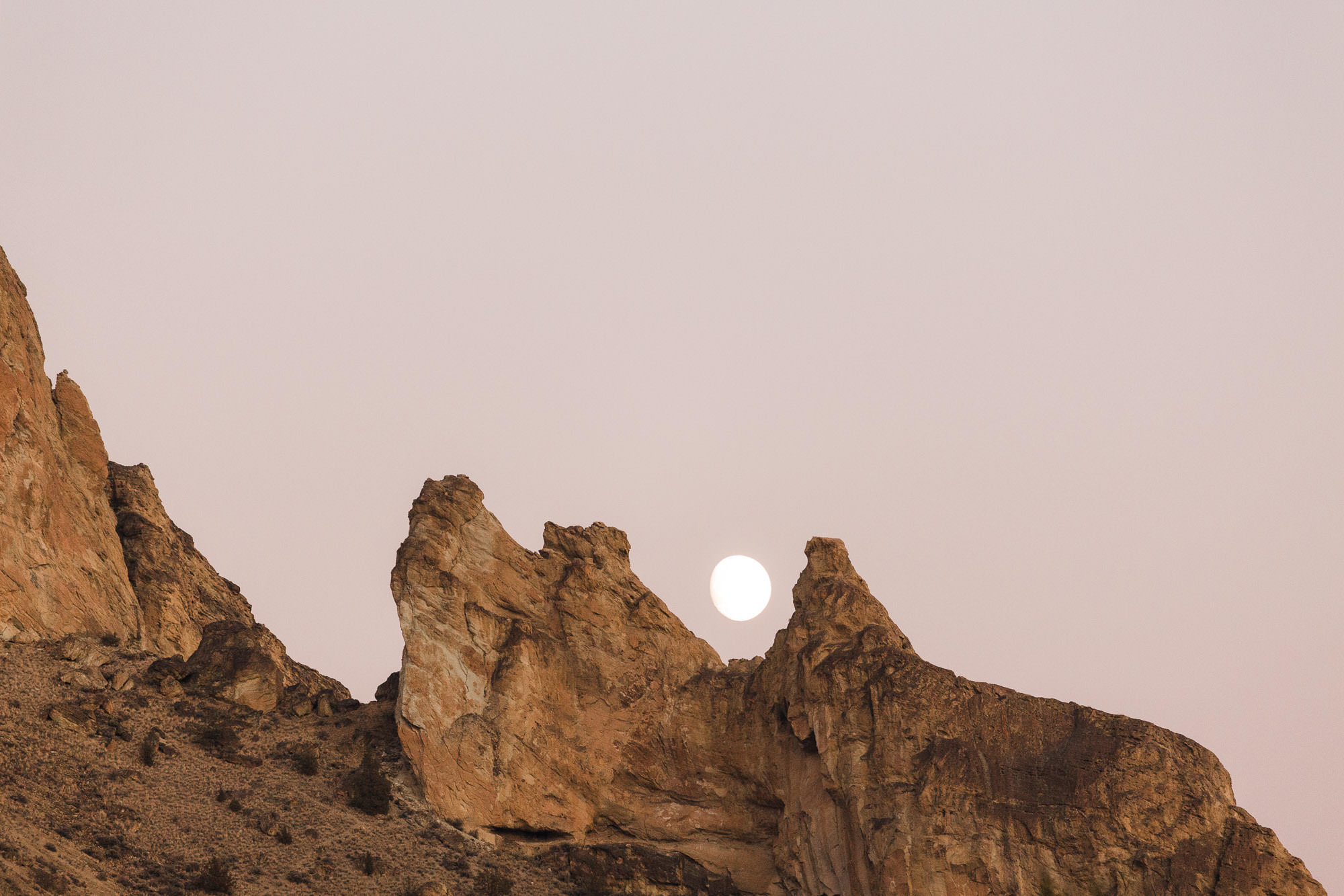 The moon sets between two rock spires at Smith Rock State Park