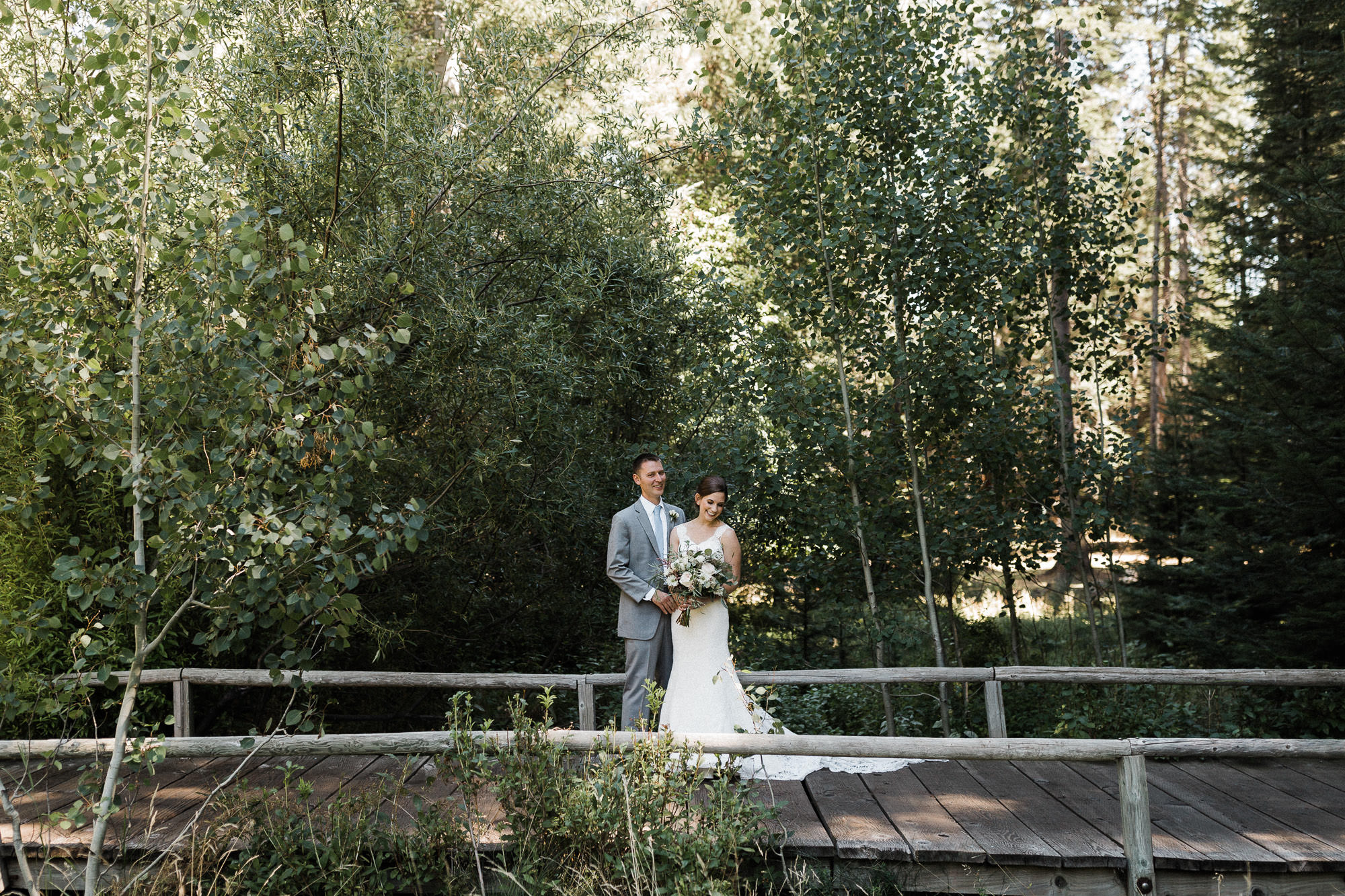 Bride and groom laugh while posing on a boardwalk in the woods at Black Butte Ranch