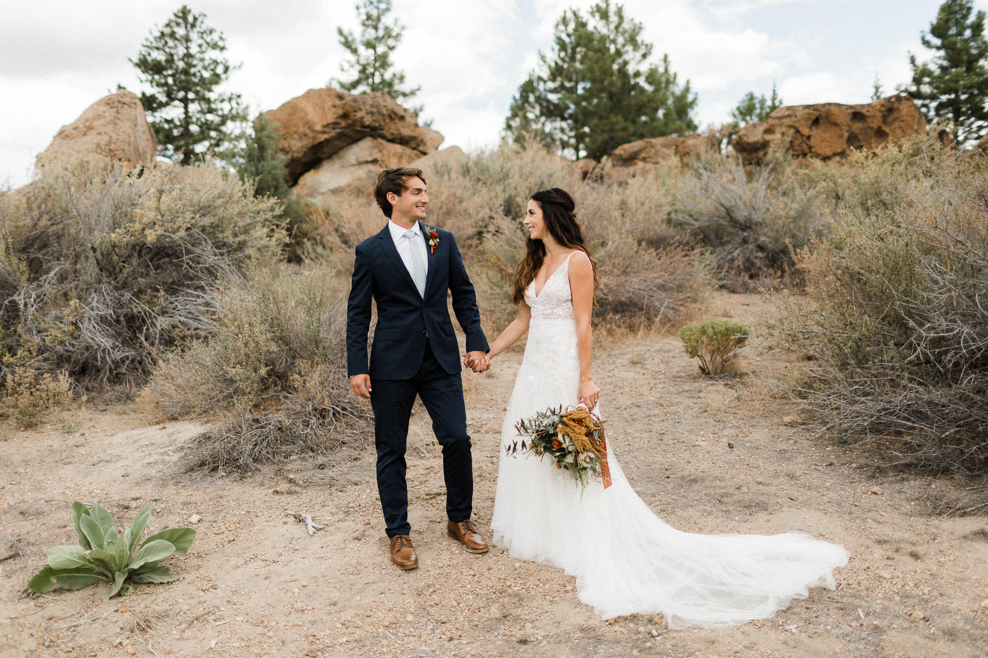 Bride and groom hold hands in desert at Broken Top Club in Bend, Oregon