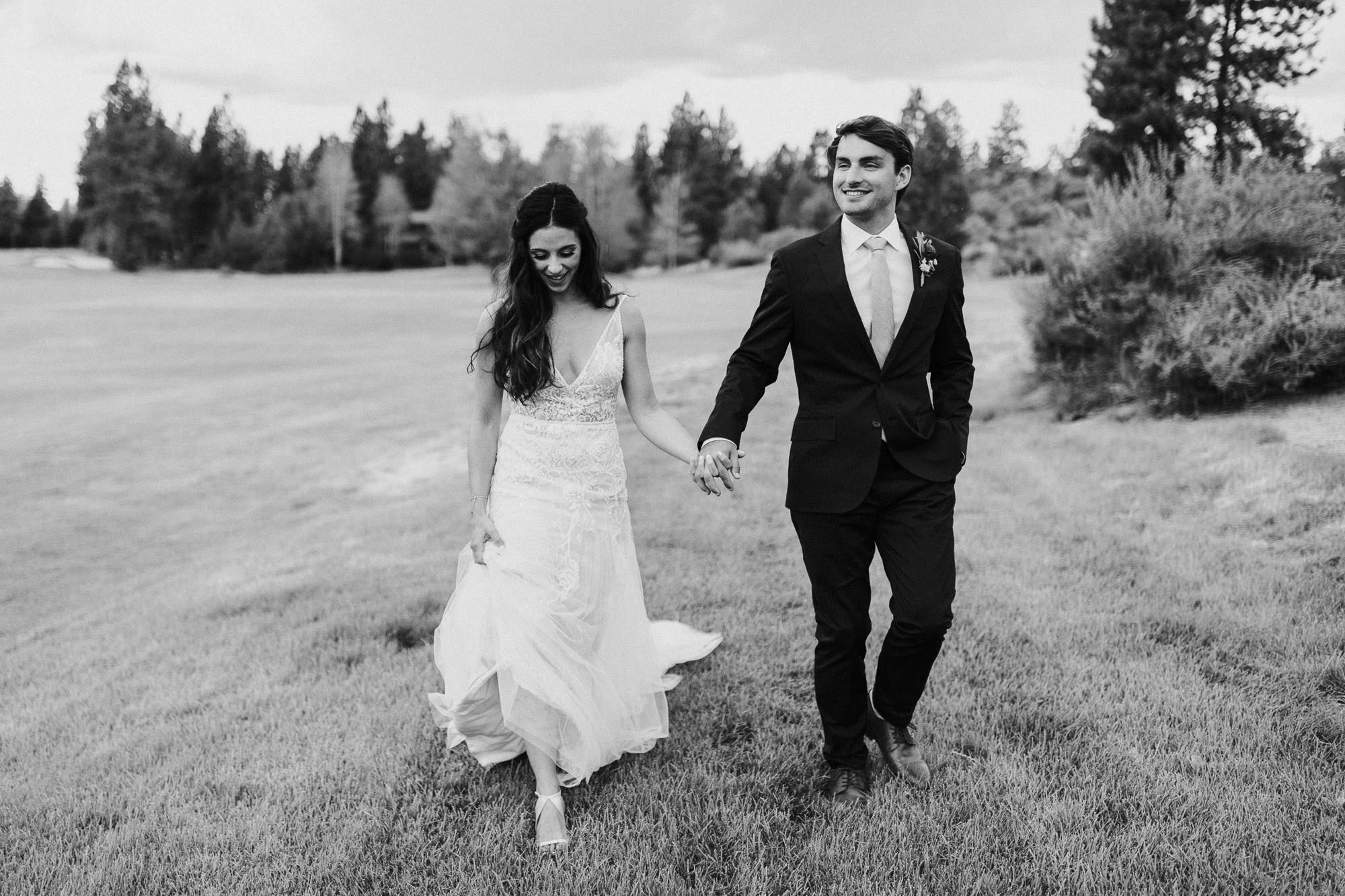 Bride and groom walk and hold hands at Broken Top Club in Bend, Oregon