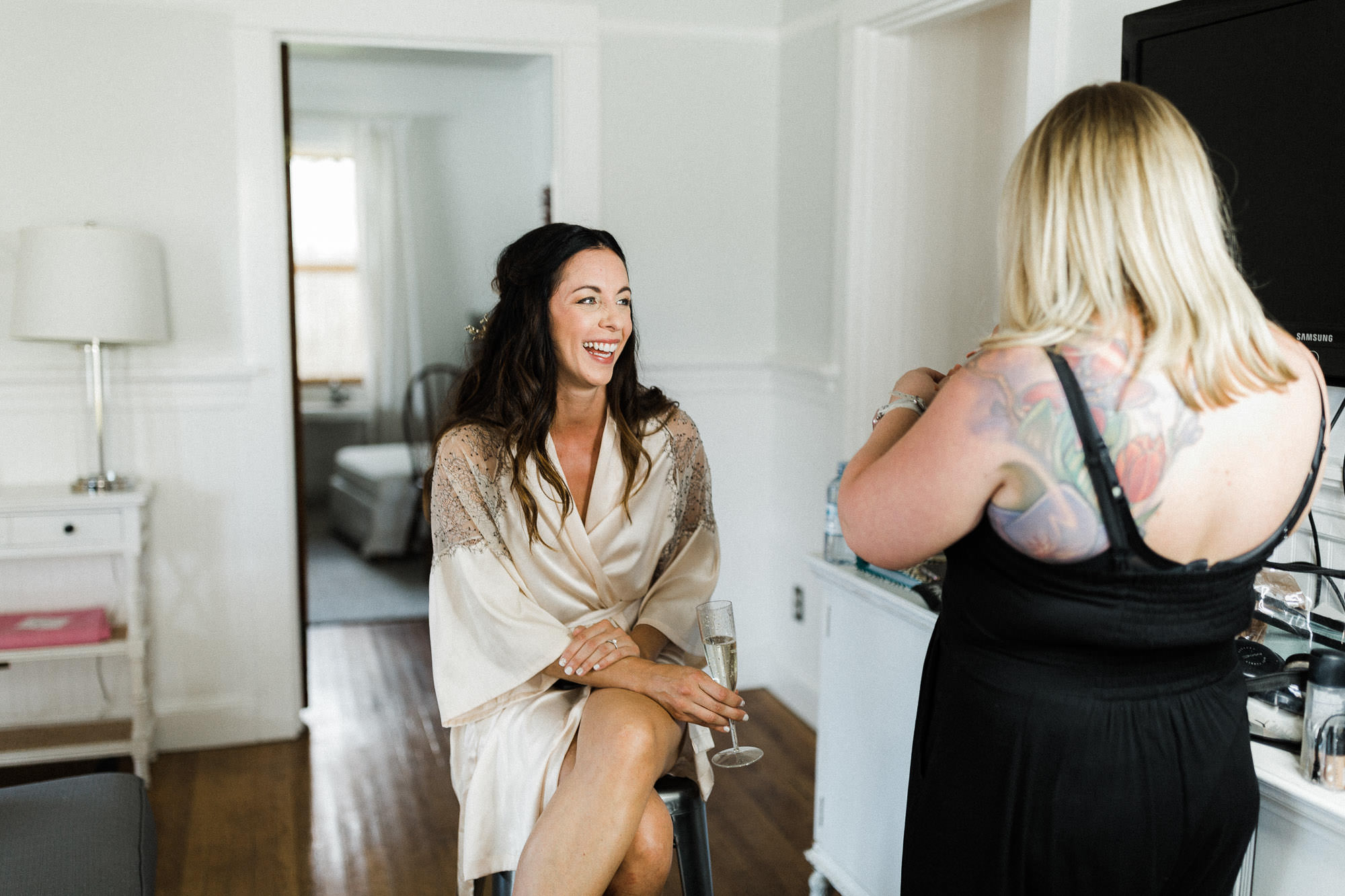 Bride laughing, drinking bubbly while getting makeup done in Bend, Oregon