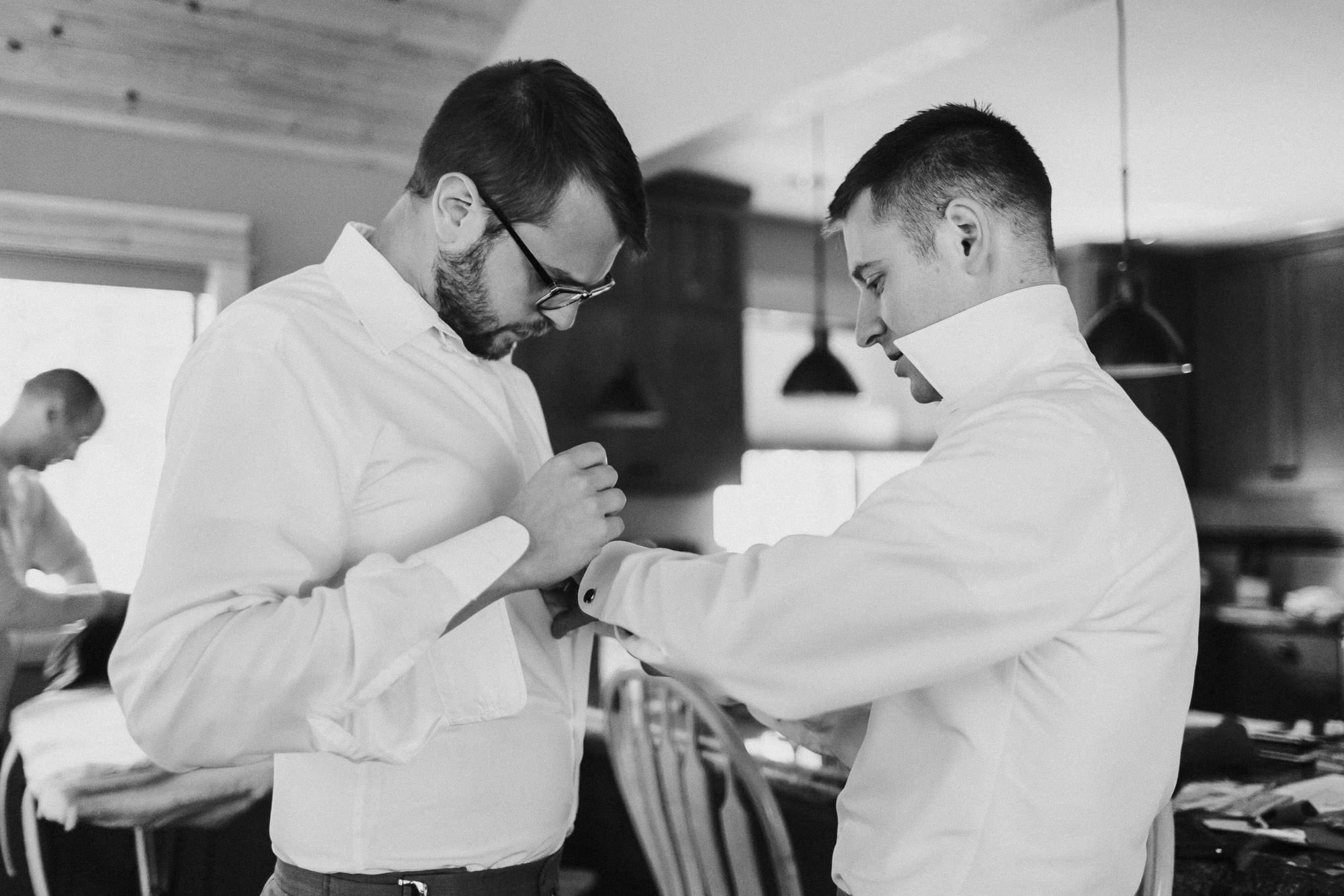 Groom helps groomsman button his shirt at Black Butte Ranch