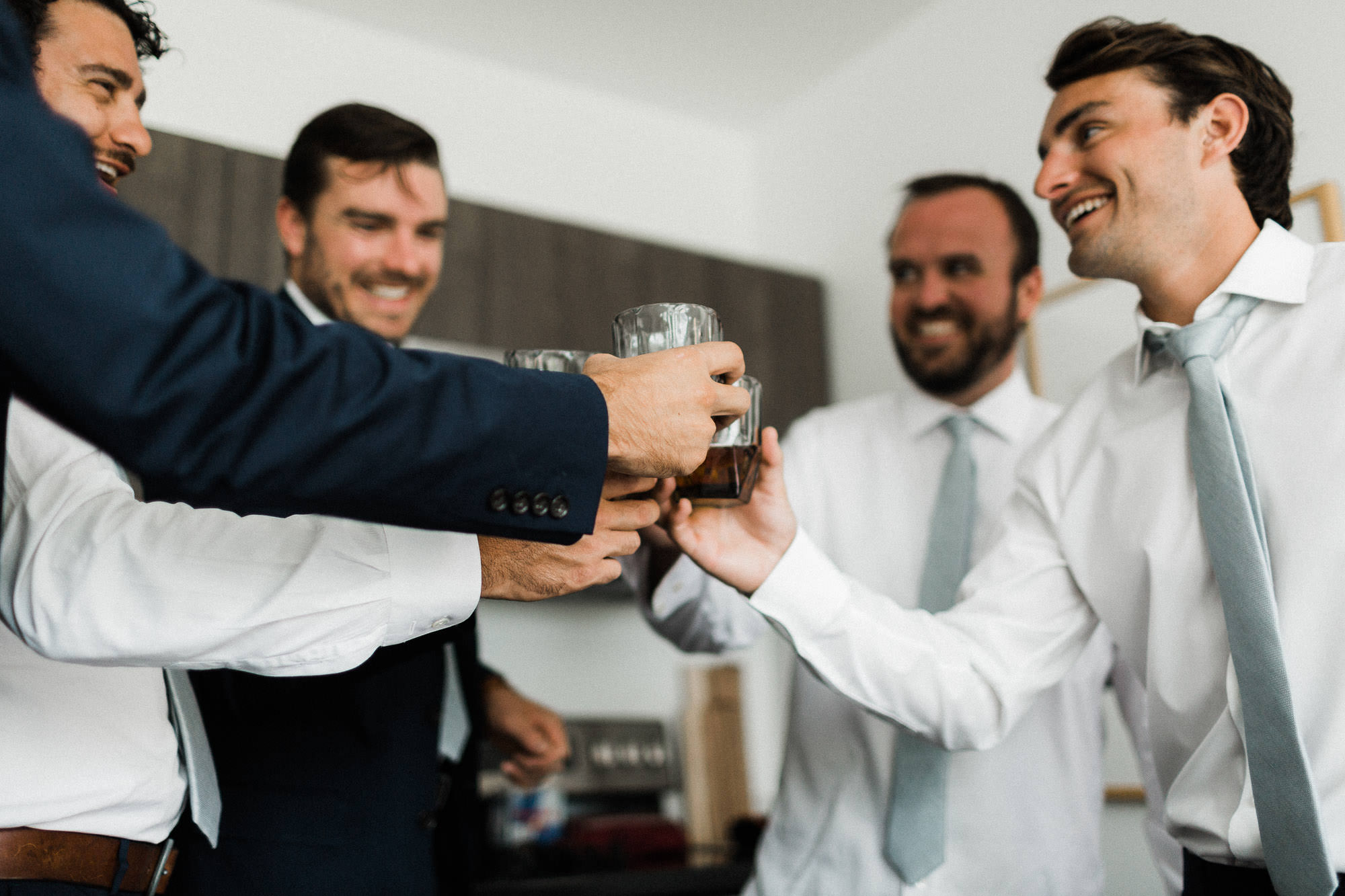 Groom and groomsmen clink glasses of whiskey in a cottage in Bend, Oregon