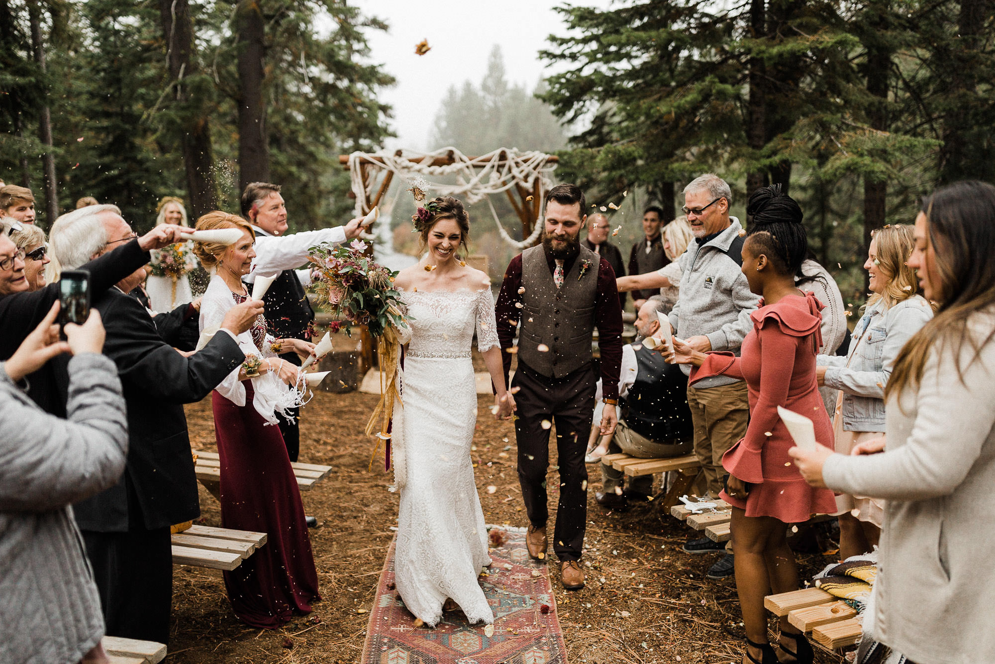 Bride and groom walk down the aisle as guests toss dried flowers at Skyliner Lodge