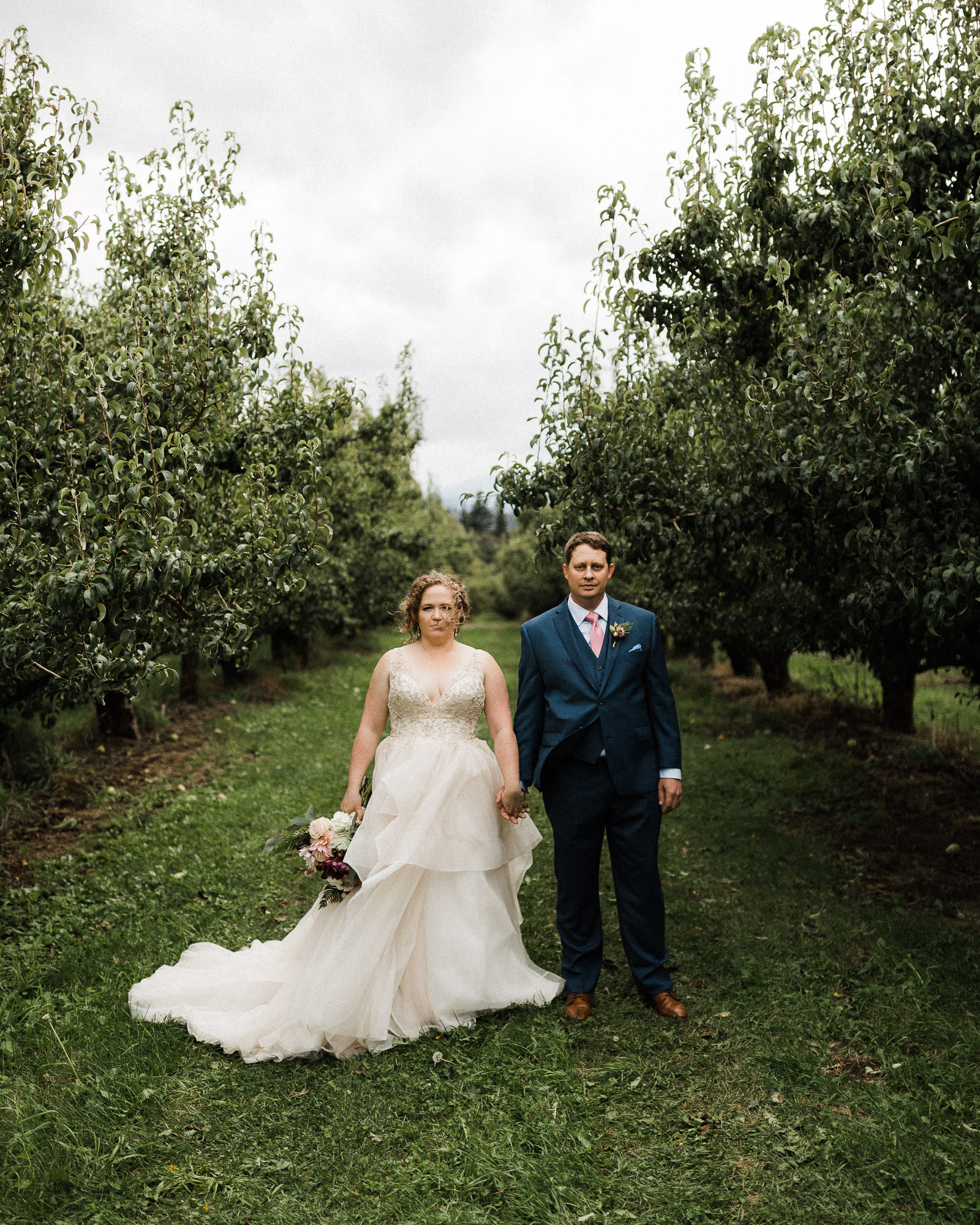 Bride and groom hold hands in an orchard row at Mt. View Orchards.