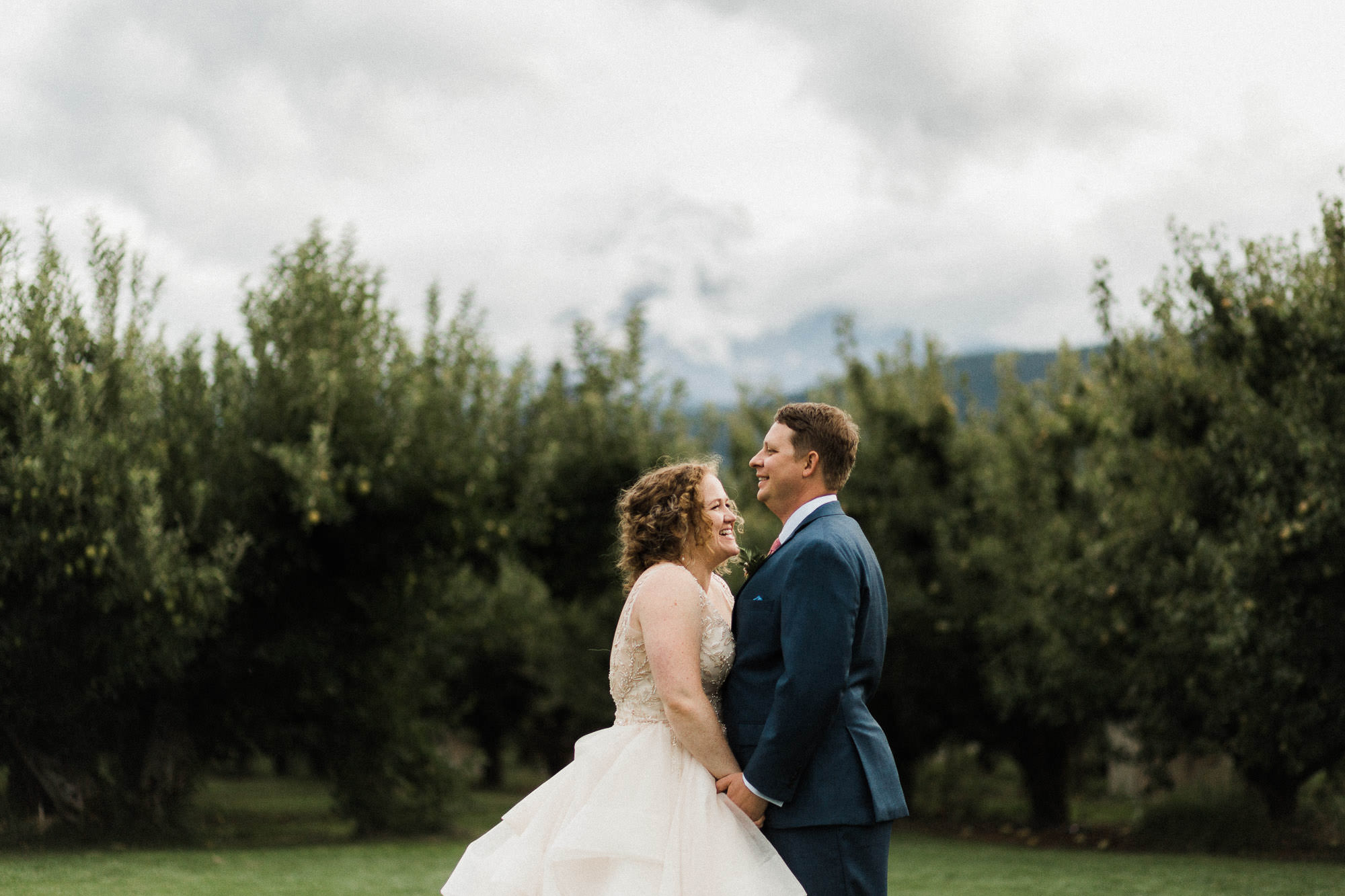 The bride and groom laugh together with Mt. Hood peeking out from clouds in the background.