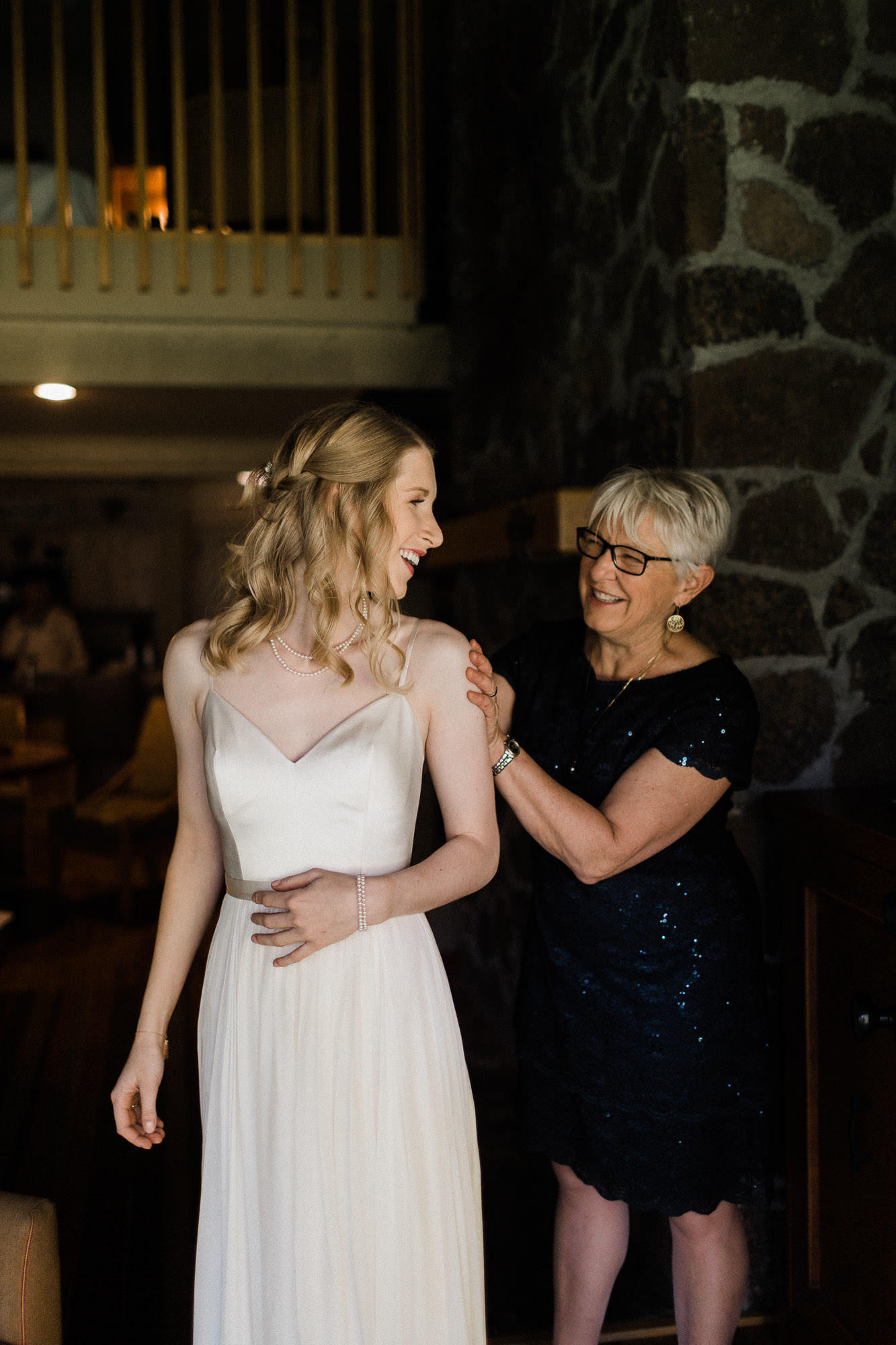 The mother of the bride helps the bride with her dress.