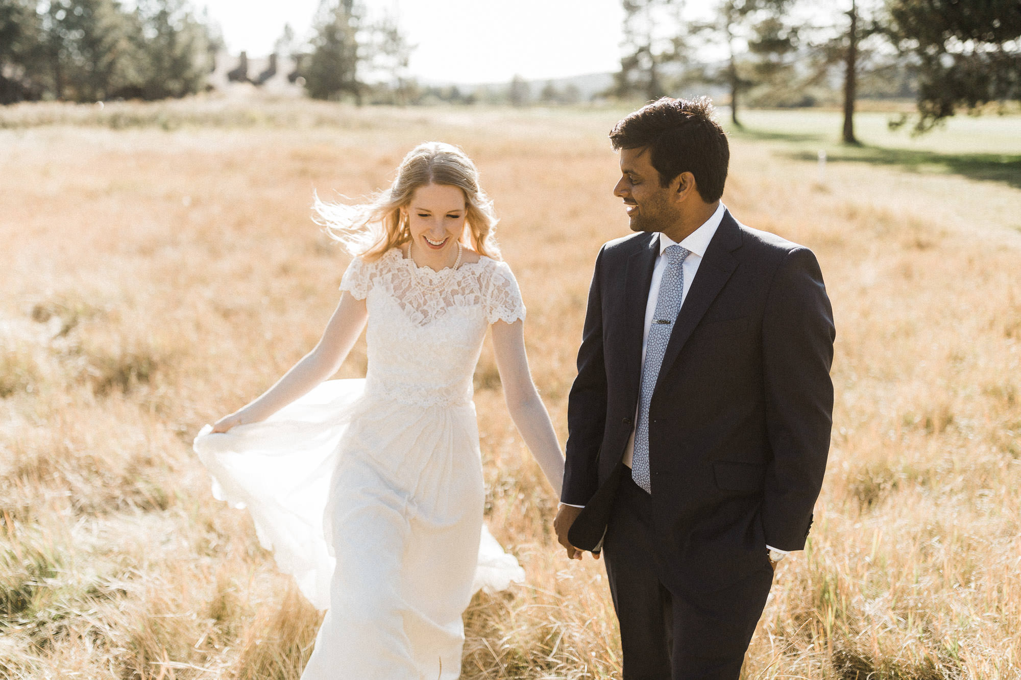 Bride and groom hold hands and walk through tall grass at Sunriver Resort in Oregon