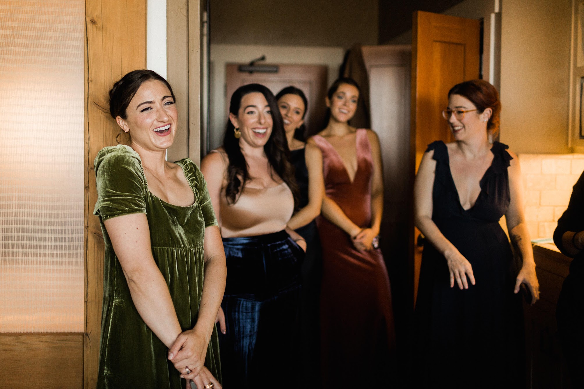 The bridesmaids all in velvet dresses looking at the bride and smiling 
