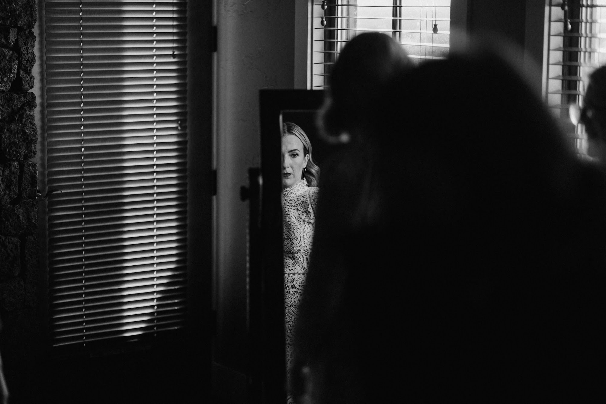 The bride looking at her self in the mirror while her mother buttons up her dress. 
