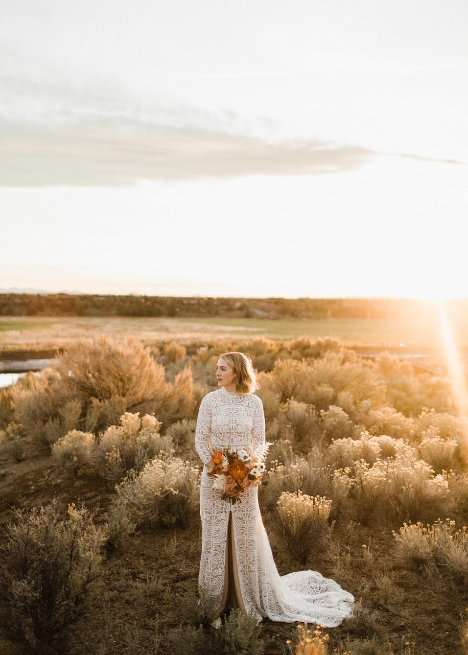 golden hour photo of the bride standing alone in a field surrounded by the high dessert