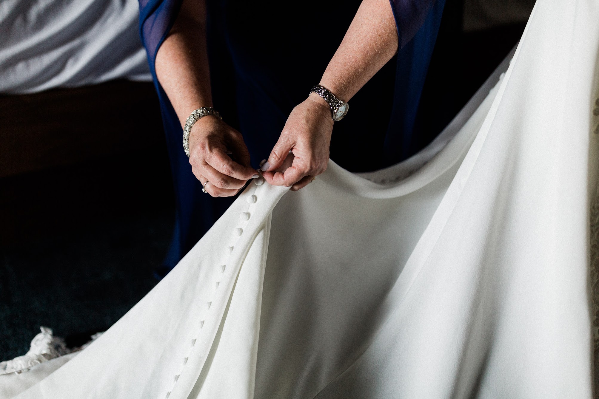 a beautiful lace wedding gown being buttoned by mom