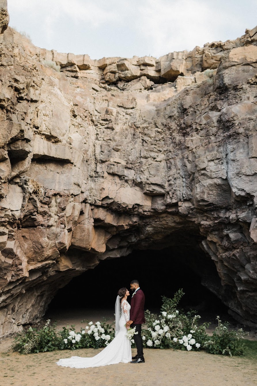 the couple standing in a cave with a floral install coming up from the ground.