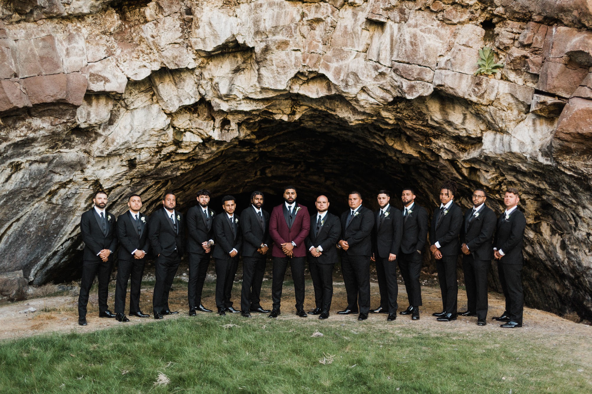 the groomsmen all lined up in front of a cave.