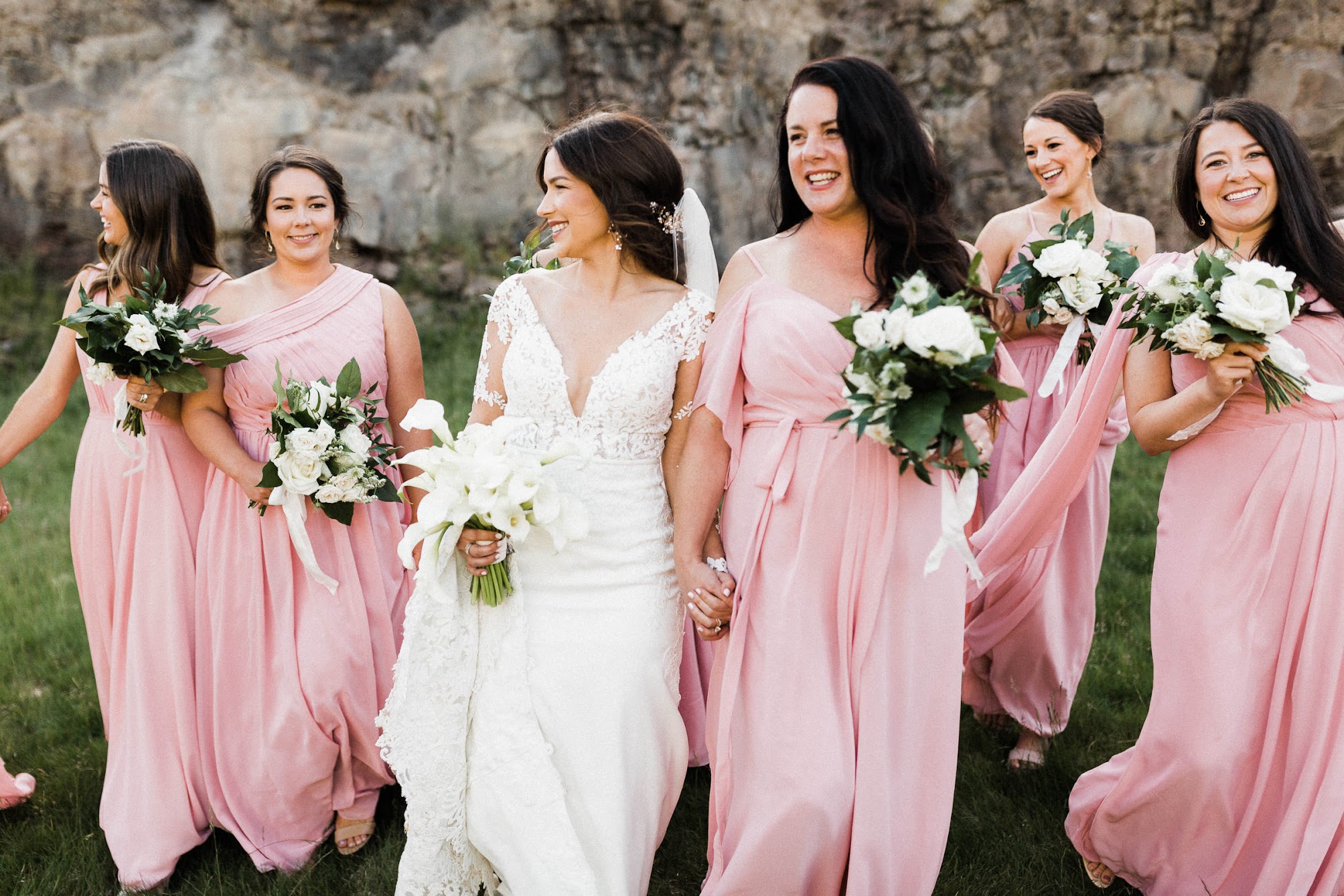 Bride is holding hands with her maid of honor while the other bridesmaids walk behind them.  