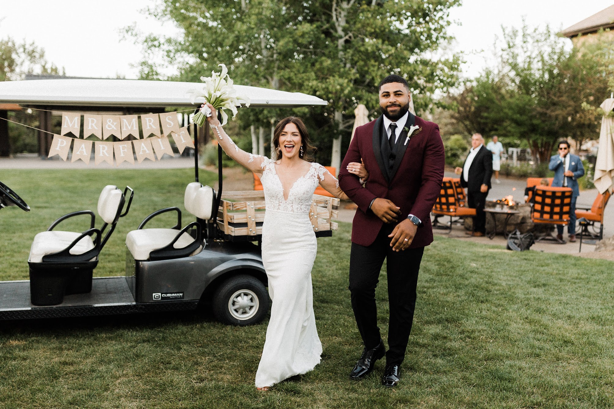 bride and groom walking into their wedding reception, behind them, a golf cart that says "Mr. & Mrs. Parfait"