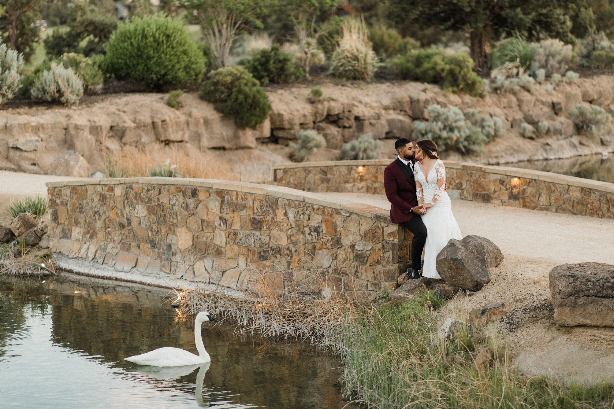 the couple sitting on a Tuscan like bridge, while kissing and a adult swan is swimming by