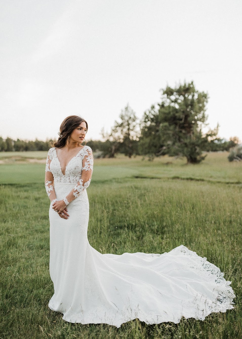 The bride standing in a grassy field with her dress train completely laid out