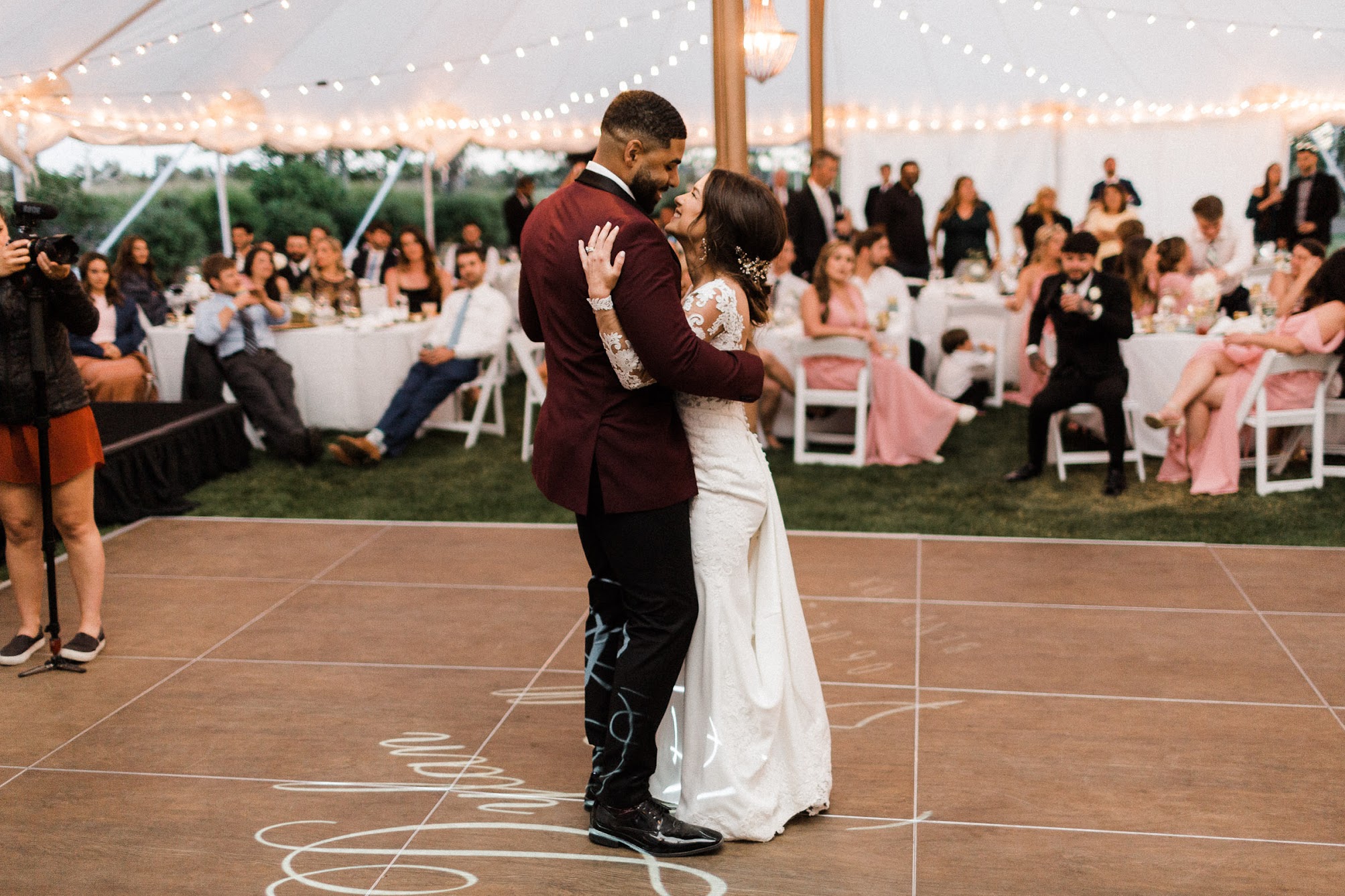 the couple dancing on the dance floor, under a tent that has bistro lighting. 