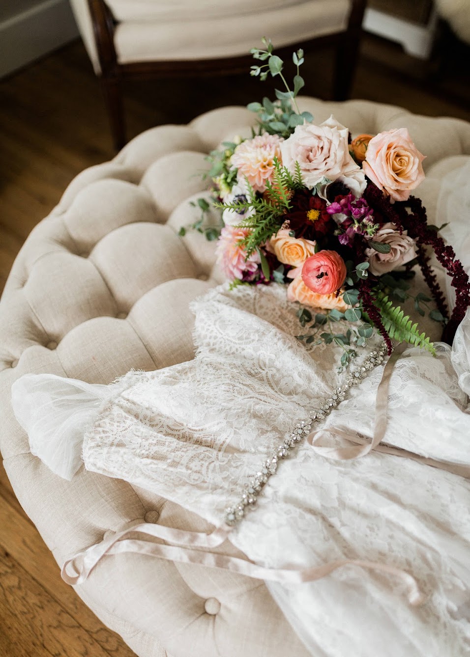 Bride's dress laying on a couch with next to the bridal florals