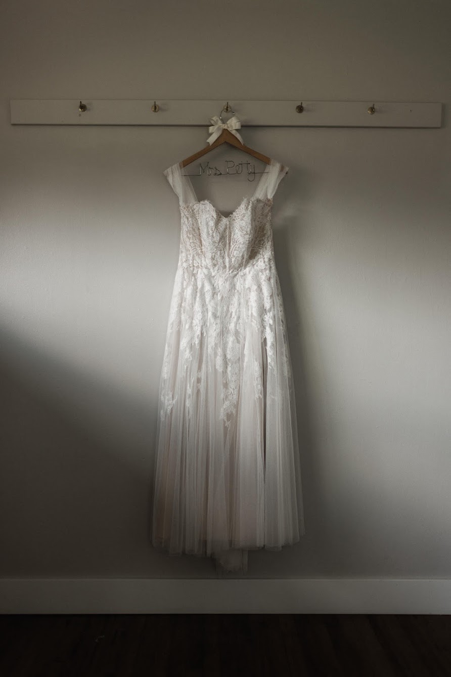 Long sleeveless wedding dress hanging on a hanger with a cute white bow