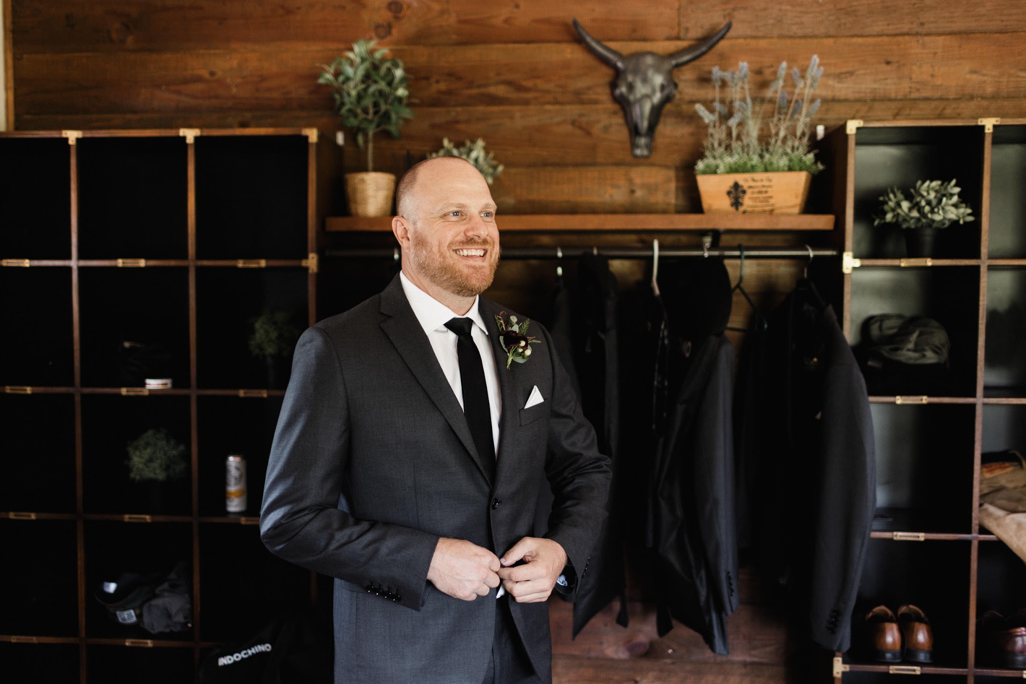 Groom buttoning up his suit jacket with a big smile on.