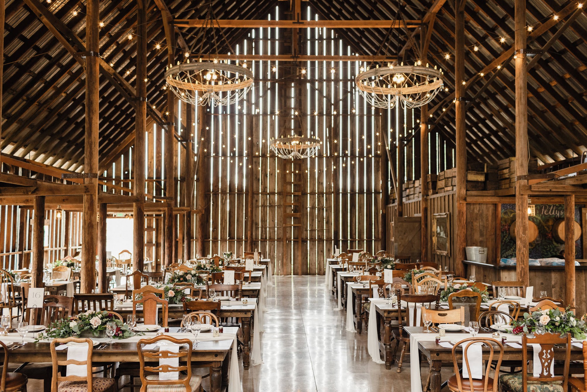 Three large chandeliers hanging in a large barn with bistro lights
