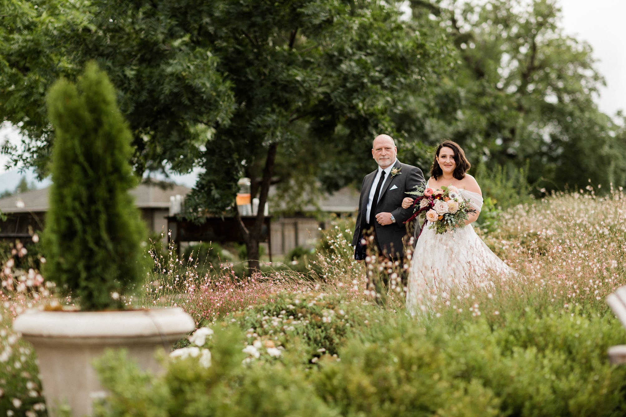 The bride and her father with locked arms walk down the stunning aisle that has natural flowers lining it. 