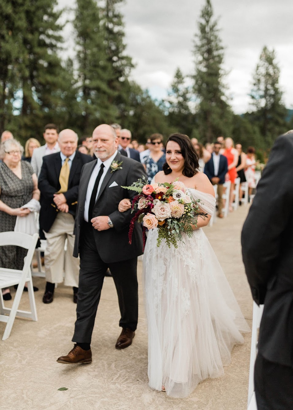 The bride and her father reach the top of the aisle, all of the guests are standing and watching them.