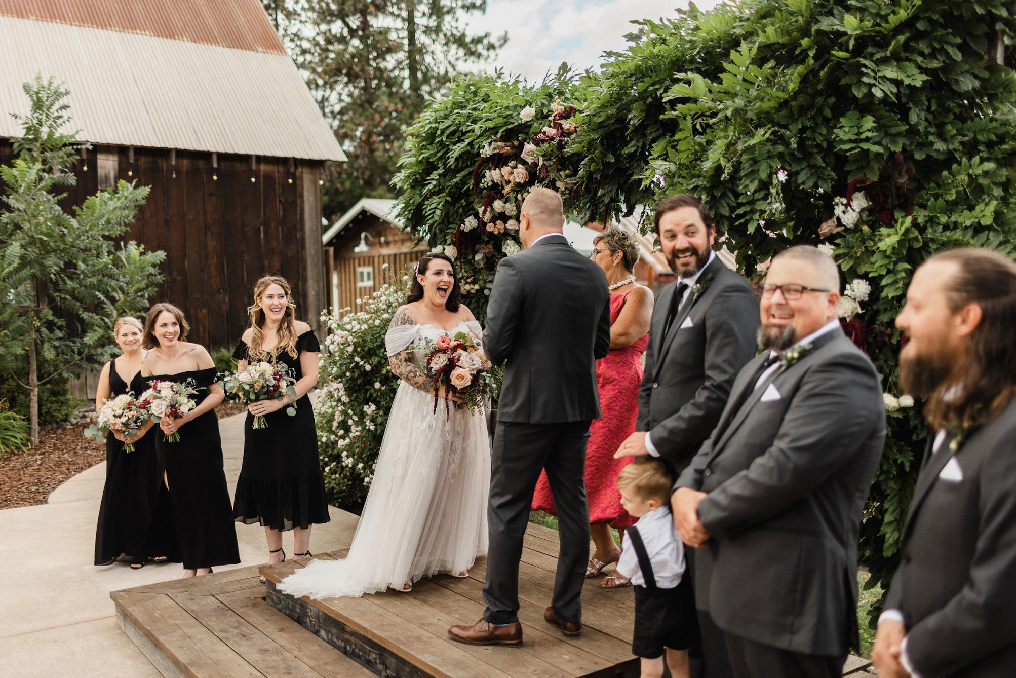 The whole bridal party, three bridesmaids and three groomsmen, bride and groom and the officiant laughing during the ceremony.  