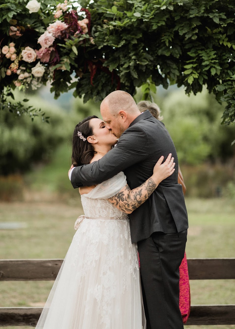 The bride and groom hugging and kissing each other under their floral arbor. 