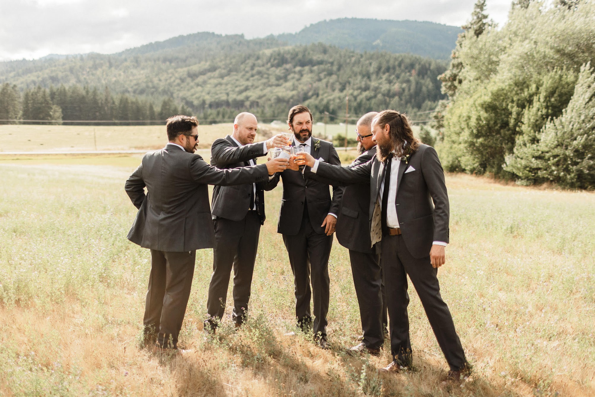 The groomsmen standing in an open field saying "cheers" with their beers