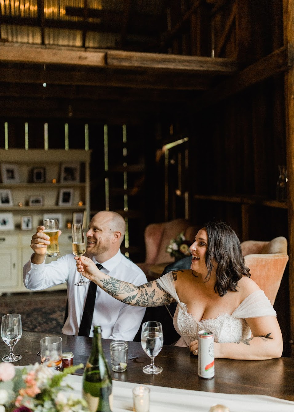 The couple sitting at their table holding up and cheering with a glass of beer and  Champagne.