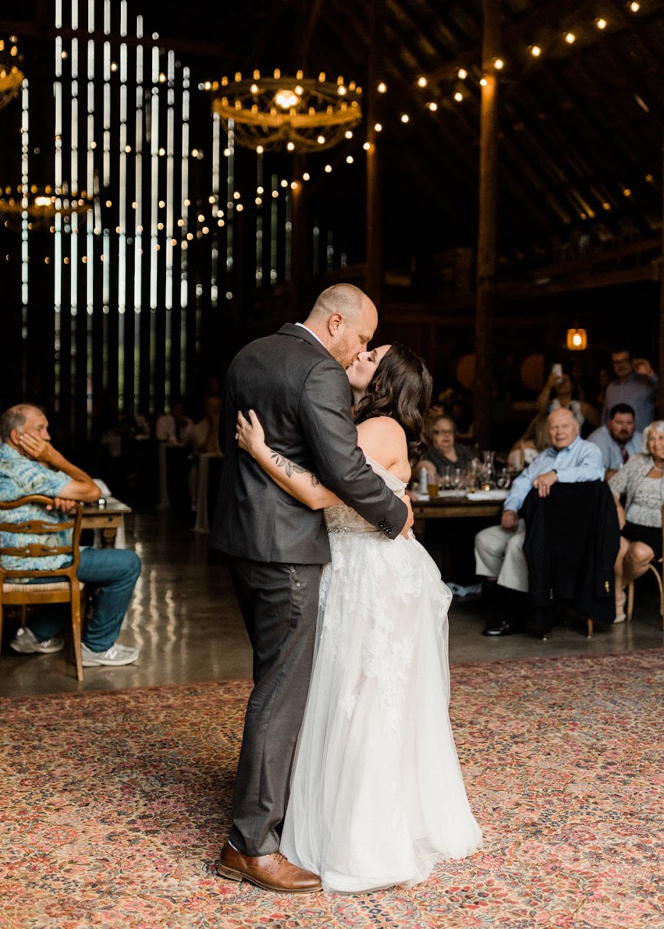 the couple standing in the middle of the dance floor kissing while their guests are sitting.