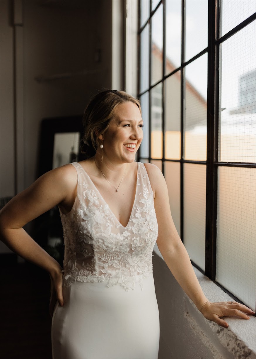 bride laughing while looking at the window, with her hand on her hip. 