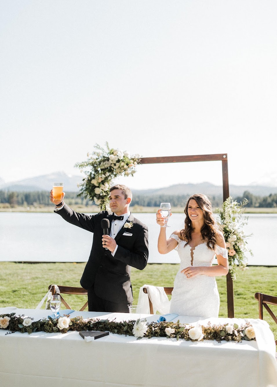 Bride and groom at their sweetheart table holding up drinks 