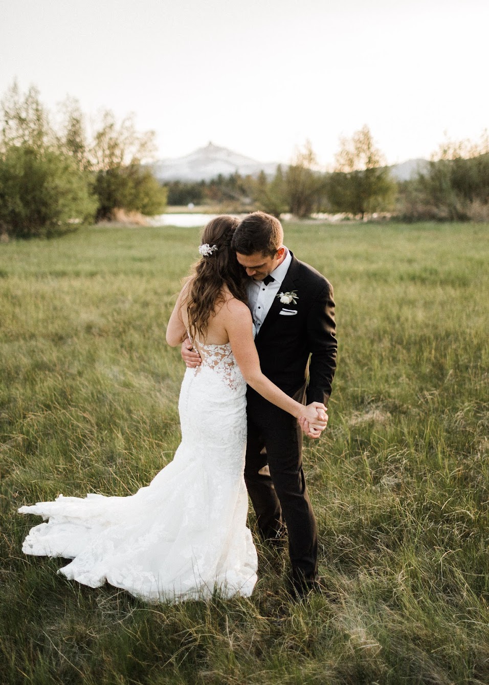 bride and groom slow dancing in a field with a mountain view behind them
